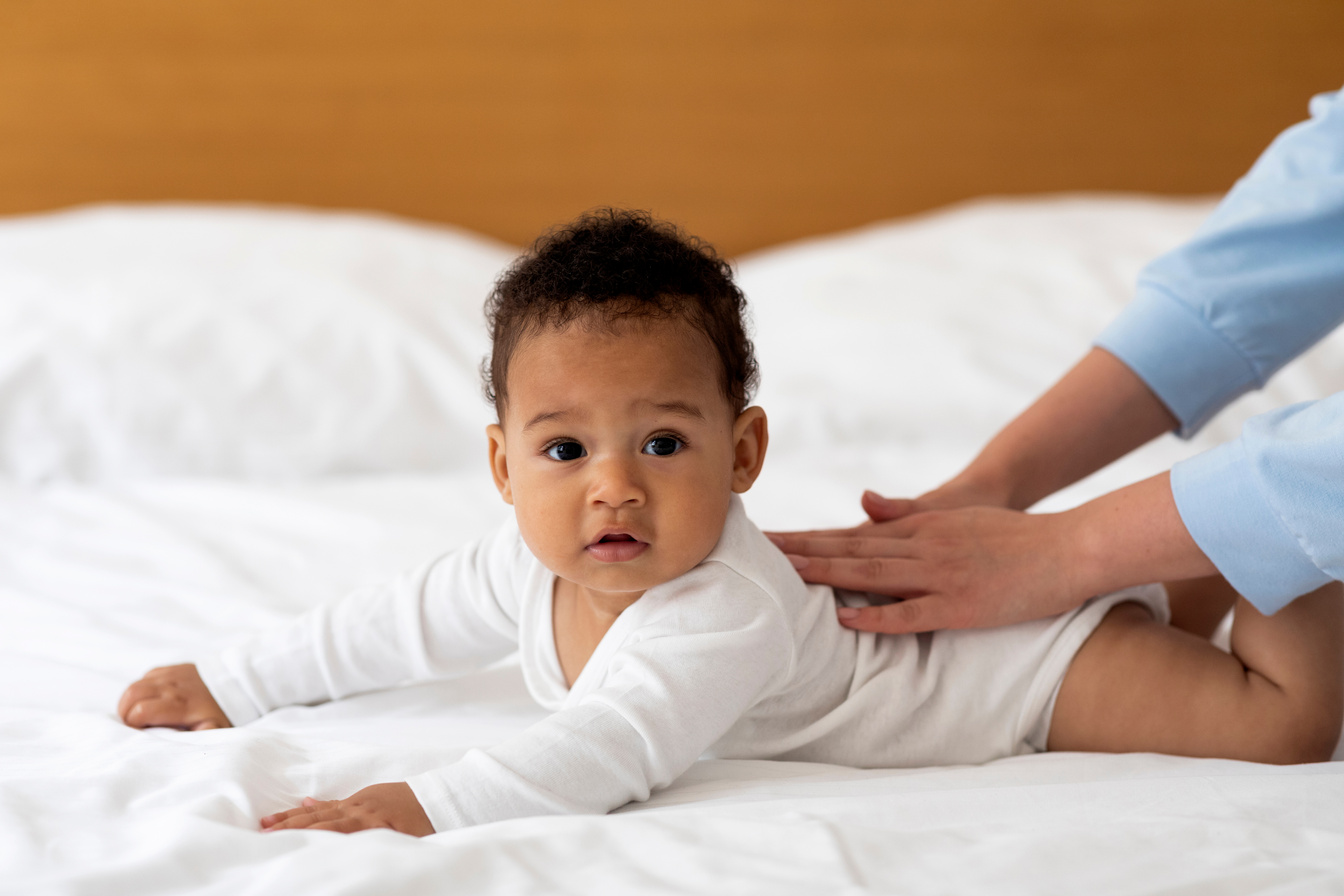 Parent Massaging the Back of a Baby on the Bed